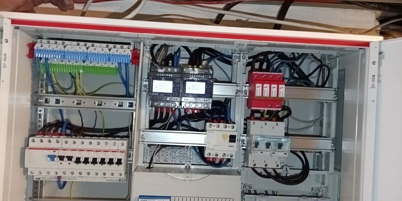 Otwarta szafa rozdzielcza z kompletnym okablowaniem, zabezpieczeniami i modułami pomiarowymi. Widoczne elementy instalacji elektrycznej wewnątrz obudowy.