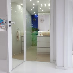 TupTech - Nowoczesna, biała łazienka z szklanymi drzwiami i fototapetą z motywem tropikalnej plaży, widoczna umywalka nablatowa i szafka z szufladami.