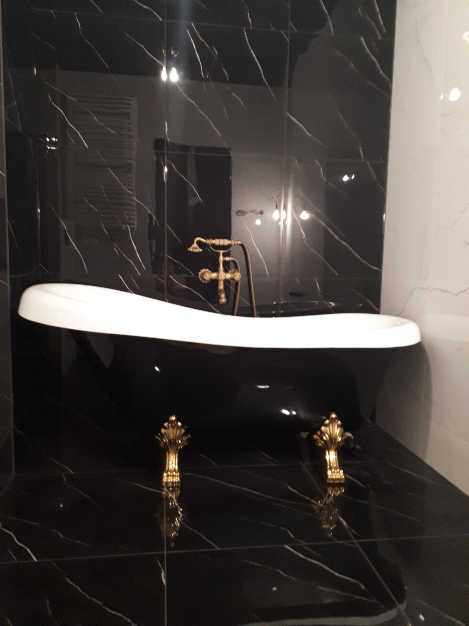 Elegancka, wolnostojąca wanna w czarno-białej łazience z marmurowymi płytkami i złotą armaturą.