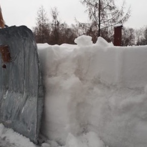 Metalowa łopata odgarnia grubą warstwę śniegu z dachu, widoczne drzewa w tle.