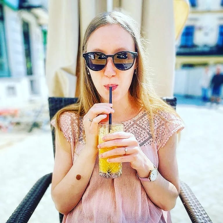 Kobieta w okularach pije sok pomarańczowy przez słomkę w kawiarni na zewnątrz.