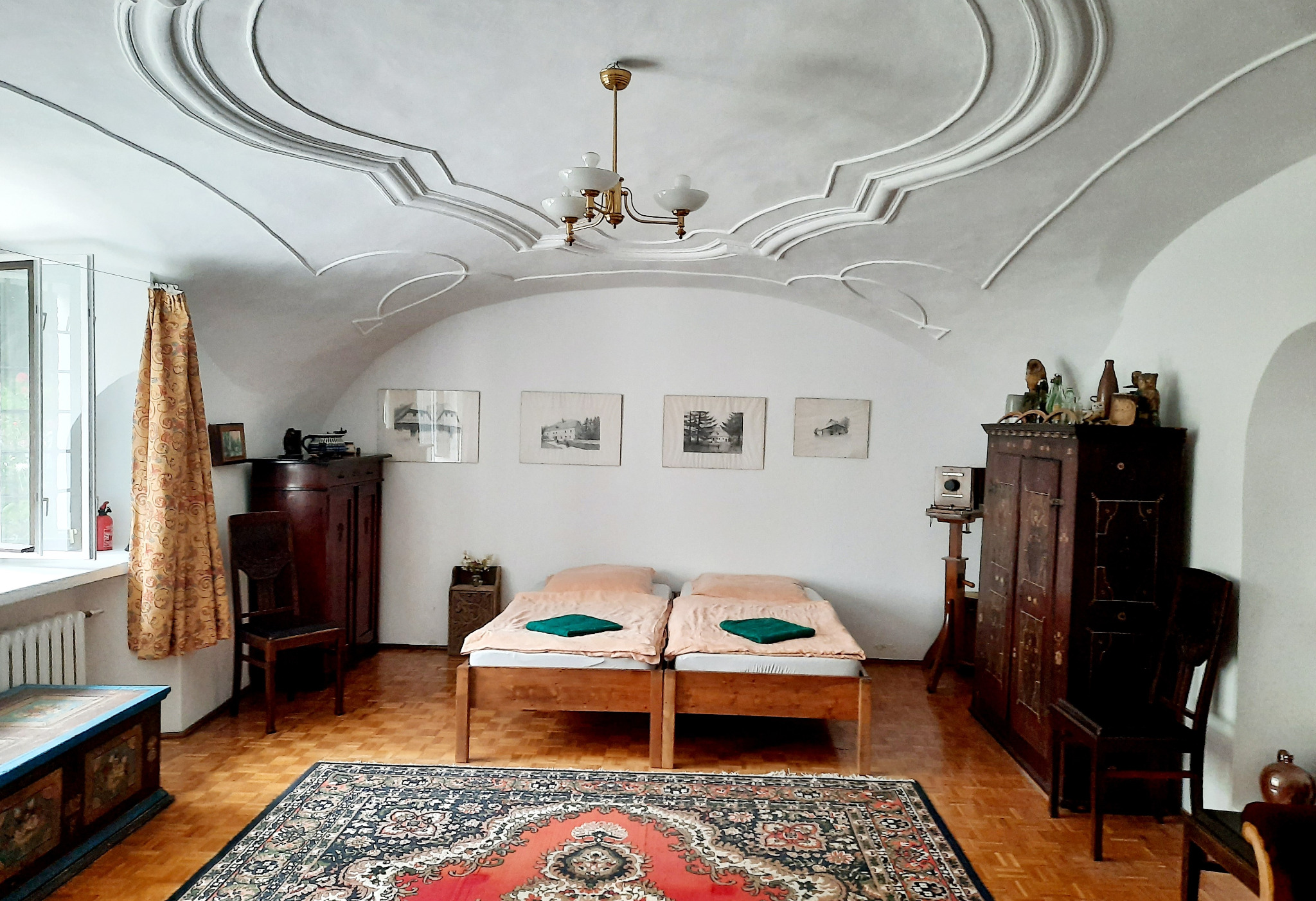 Pokój w stylu retro z dwoma łóżkami pojedynczymi, ozdobnym sufitem z gipsowymi zdobieniami, zabytkowymi meblami i dywanem orientalnym.