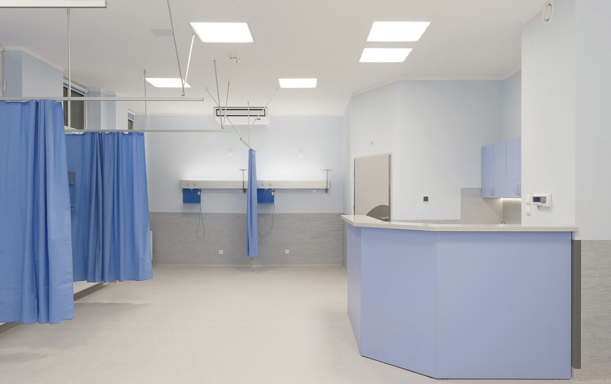 Jasne, przestronne wnętrze gabinetu lekarskiego w Szczecinie z niebieskimi zasłonami, recepcją i szafkami, sfotografowane z szerokiego kąta.