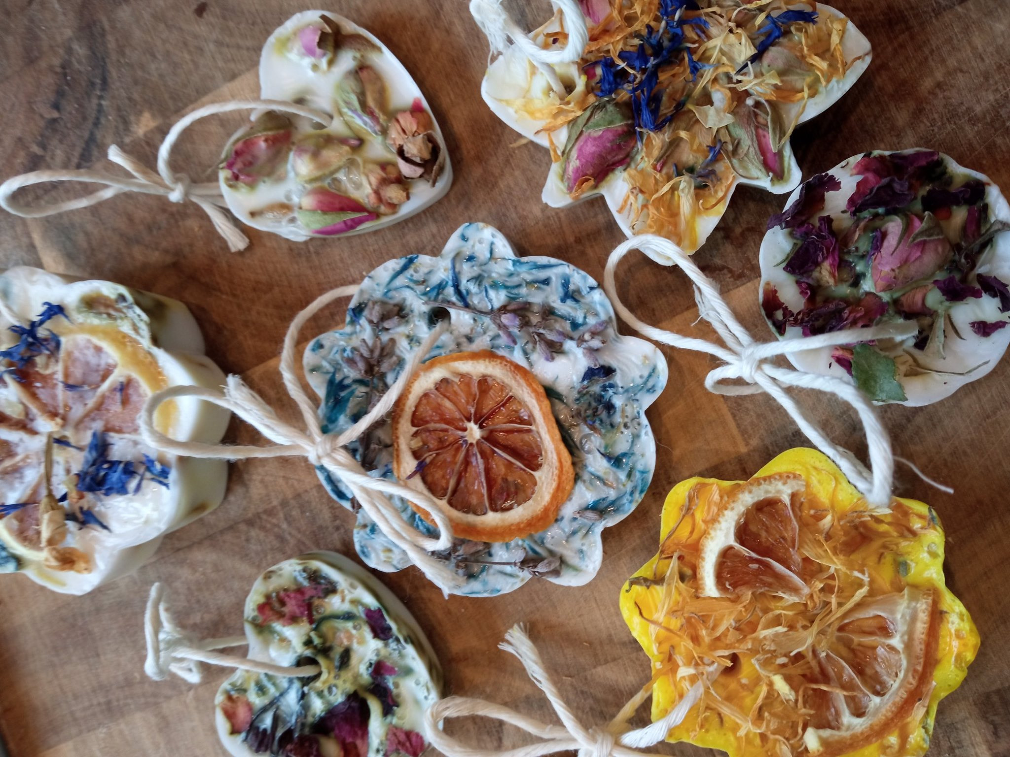Ręcznie robione zawieszki zapachowe z naturalnymi dodatkami, takimi jak suszone kwiaty i plasterki cytrusów, wykonane w Lublinie, leżą na drewnianej powierzchni.