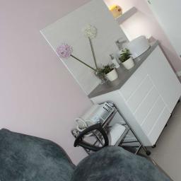 Salon Kosmetyczny OdNova - Wnętrze gabinetu: fotel zabiegowy, biała szafka z umywalką, kwiaty w wazonie i sprzęt kosmetyczny na wózku.