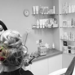 Salon Kosmetyczny OdNova - Fryzjerka upina włosy klientki z czerwonymi różami, w tle półki z kosmetykami i akcesoriami w sterylnym, jasnym wnętrzu.