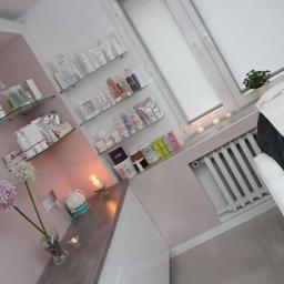 Salon Kosmetyczny OdNova - Jasne wnętrze gabinetu kosmetycznego z szarym fotelem do zabiegów, półkami z kosmetykami i dekoracjami, w tym kwiatami w wazonie i świecami.