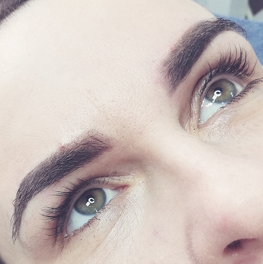 Zbliżenie na twarz kobiety z widocznym makijażem permanentnym brwi i wydłużonymi rzęsami, spojrzenie skierowane ku górze.