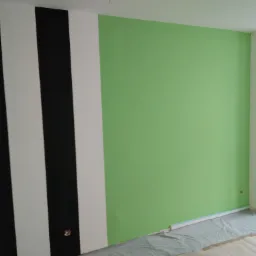 Ściana pomalowana w szerokie, pionowe pasy czerni i bieli, sąsiadująca z fragmentem ściany w kolorze jasnej zieleni; zabezpieczona folią podłoga.