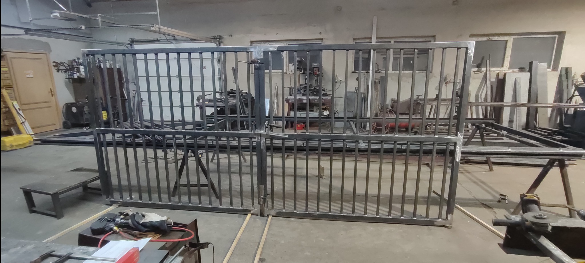 Surowe, metalowe elementy bramy wjazdowej w warsztacie, przed malowaniem. Widoczne narzędzia i stanowisko pracy, co sugeruje etap produkcji.