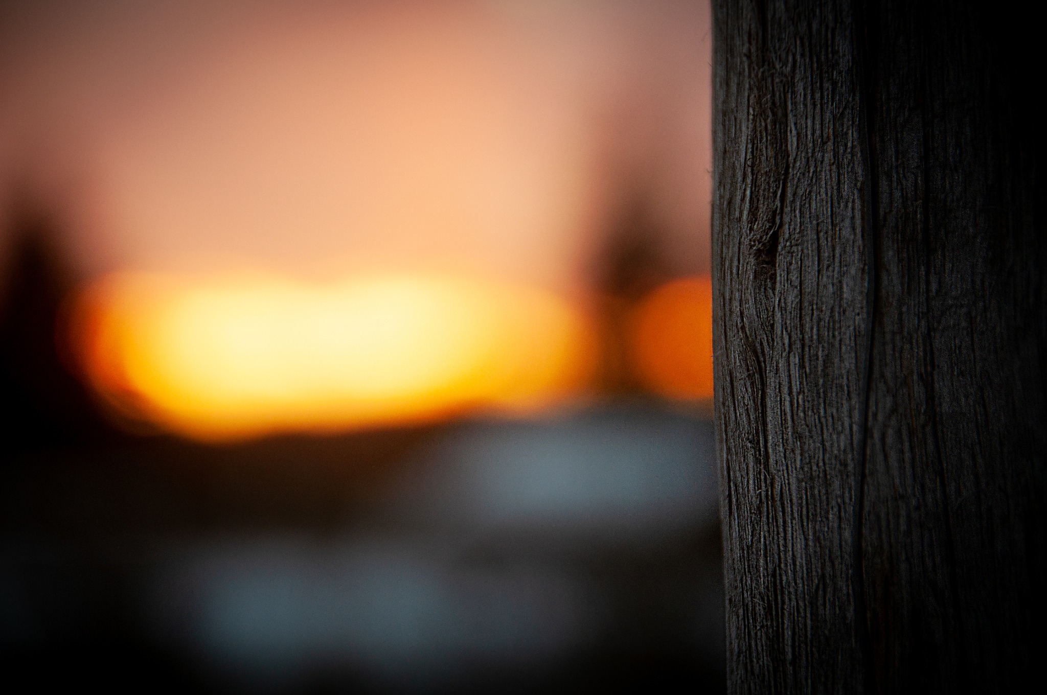 Makro zbliżenie na teksturę ciemnego, pionowego drewnianego słupka z rozmytym tłem w odcieniach pomarańczy i żółci, przypominającym zachód słońca.