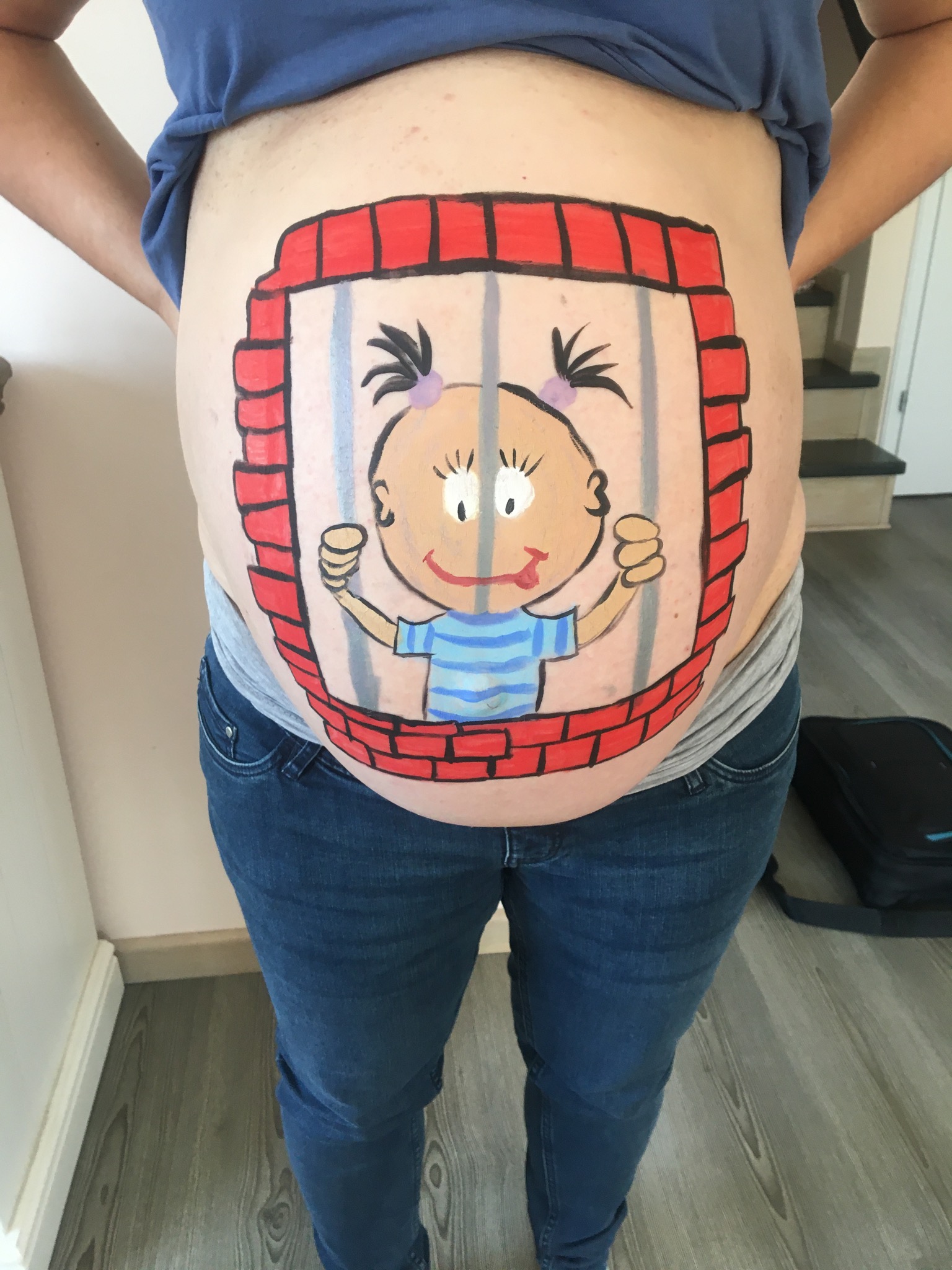 Malunek na ciążowym brzuchu przedstawia postać dziecka za kratami, wykonany farbami do ciała.