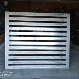 MOTO-LUK - Metalowa brama z poziomymi szczelinami, świeżo pomalowana na srebrno, widoczna w warsztacie z narzędziami i oponami w tle.