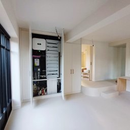 KR-Construct - Nowoczesna instalacja elektryczna w szafie wnękowej, widoczny inwerter i rozdzielnica w minimalistycznym wnętrzu z dużym oknem i podwyższoną podłogą.