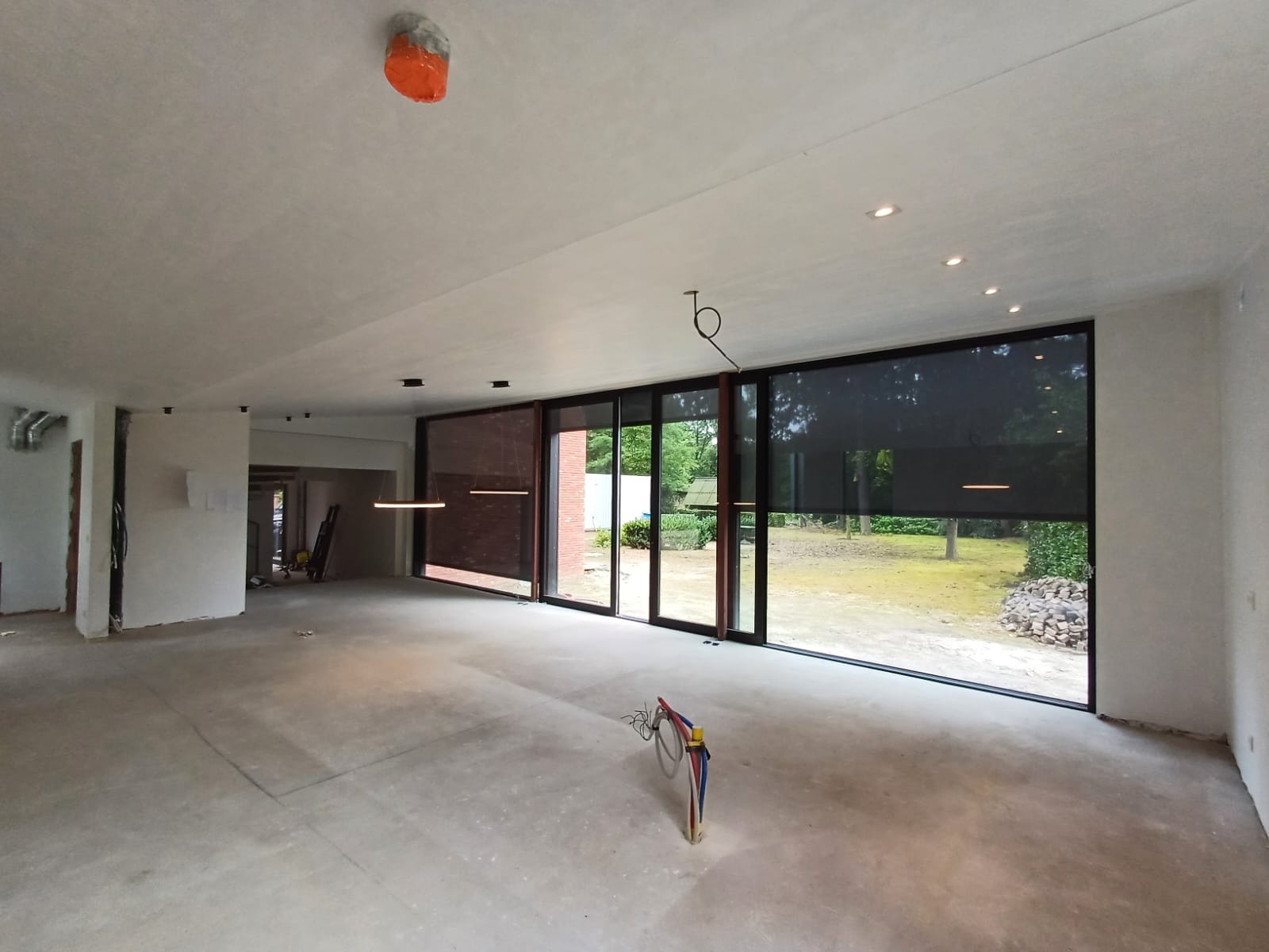 Surowy stan wnętrza z dużymi oknami i widoczną instalacją elektryczną, przygotowany do dalszych prac wykończeniowych, widoczne przewody na podłodze.