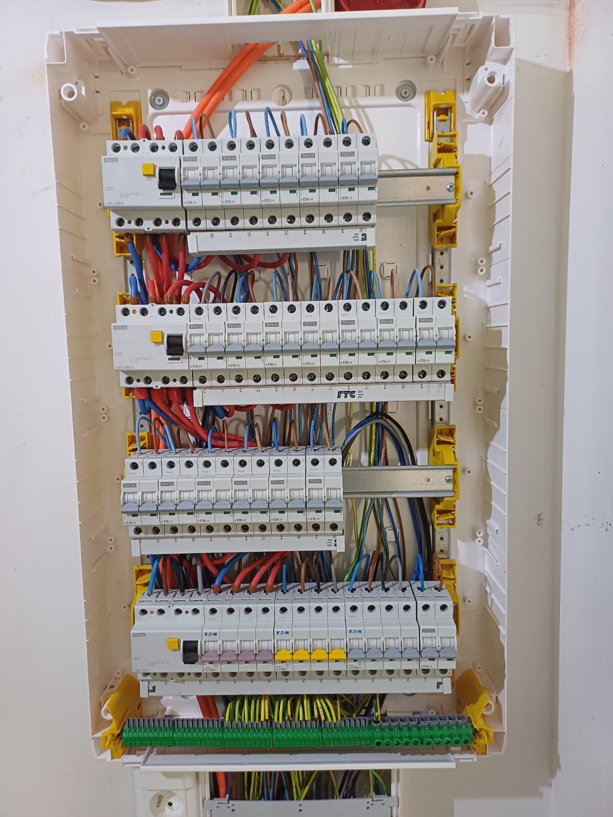Rozdzielnica elektryczna z zainstalowanymi bezpiecznikami i przewodami o różnych kolorach, zamontowana w białej obudowie na jasnej ścianie.