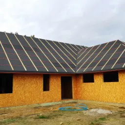 Surowa konstrukcja domu szkieletowego w Pleszewie z widocznym deskowaniem ścian i czarną membraną dachową z listwami kontrłat, przygotowana do dalszych prac wykończeniowych.