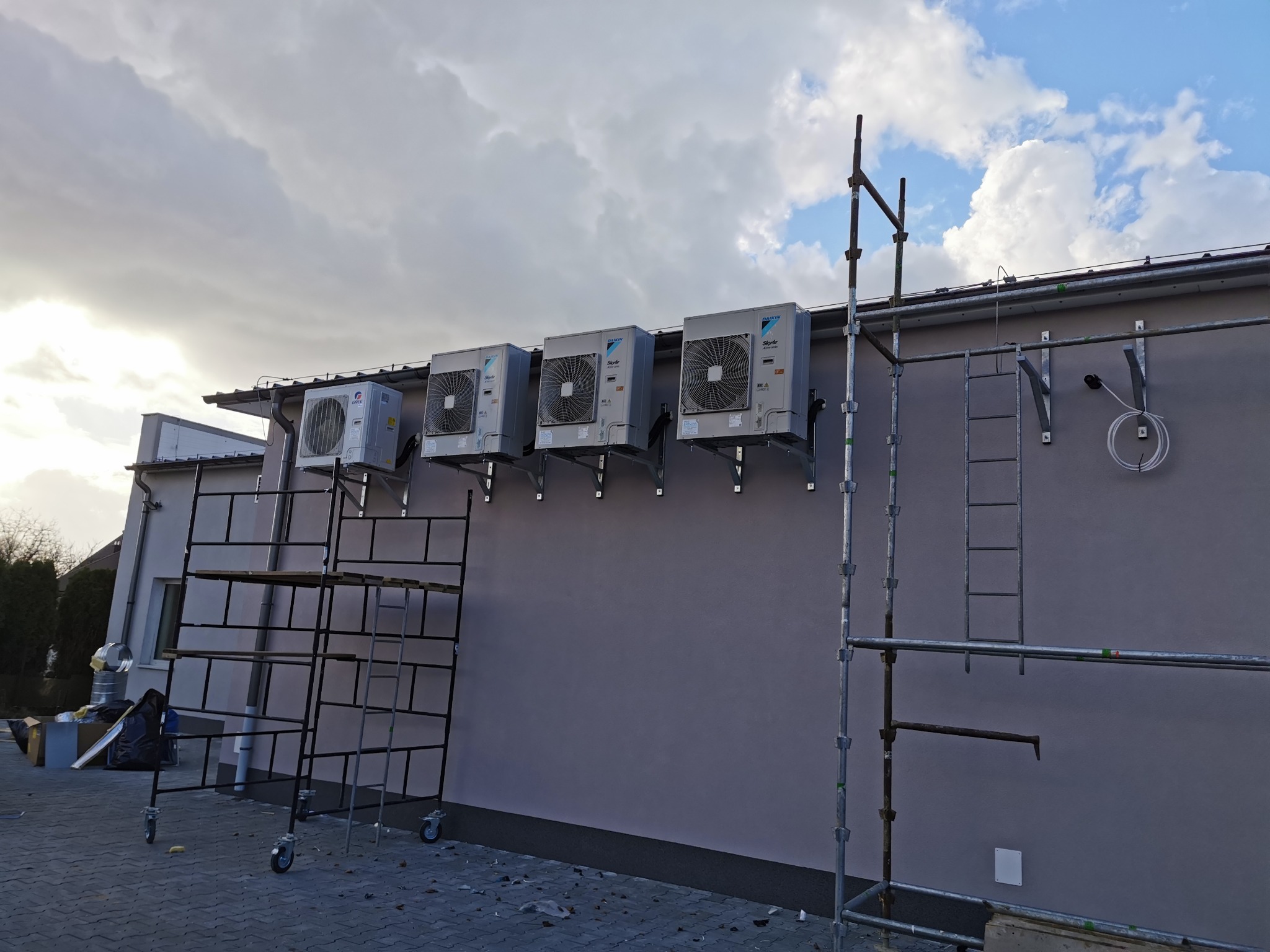 Cztery jednostki zewnętrzne klimatyzacji Daikin SkyAir zamontowane na ścianie budynku, widoczne rusztowania i przewody instalacyjne.