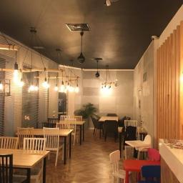 Firma ogólnobudowlana FACHDOM Jarosław Lewiński - Wnętrze lokalu gastronomicznego z drewnianą podłogą w jodełkę, stołami i krzesłami o różnym designie, wiszącymi lampami z żarówkami Edison i czarnym sufitem z kratkami wentylacyjnymi.