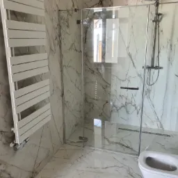 Nowoczesna łazienka z kabiną prysznicową ze szklanymi drzwiami na zawiasach, grzejnikiem drabinkowym i toaletą w marmurowym wykończeniu.