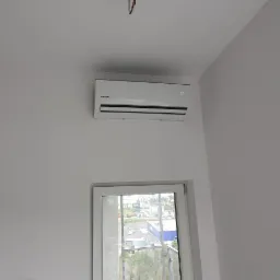 Biały klimatyzator marki Kaisai zamontowany na ścianie nad balkonowymi drzwiami, widoczne wystające kable ze złączkami na suficie, instalacja w trakcie realizacji.