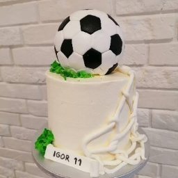 Pracownia Słodkości Carmellova - Tort z dekoracją piłkarską, zwieńczony piłką nożną, z napisem 'Igor 11' na podstawie, na tle białej ceglanej ściany.