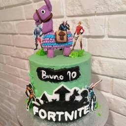 Pracownia Słodkości Carmellova - Tort urodzinowy z zielonym kremem, dekoracjami Fortnite i figurką lamy pinaty na wierzchu, umieszczony na srebrnej paterze.