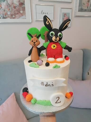 Tort urodzinowy z figurkami Binga i Flopa, dekorowany kolorowymi kulkami i napisem #Adaś, na srebrnej paterze.