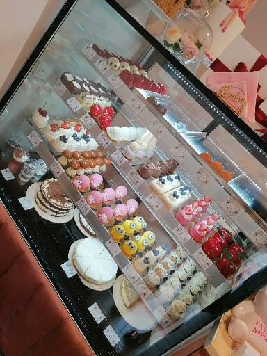 Słodka ekspozycja: torty, babeczki i desery w szklanej witrynie cukierniczej, z różnorodnymi dekoracjami owocowymi i kremowymi.