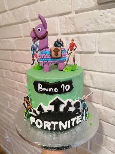 Tort urodzinowy z zielonym kremem, dekoracjami Fortnite i figurką lamy pinaty na wierzchu, umieszczony na srebrnej paterze.