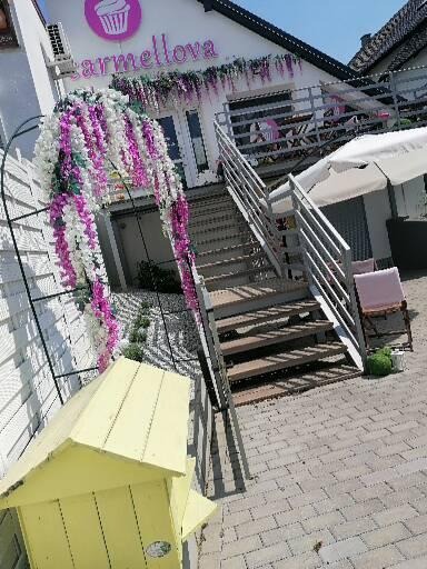Wejście do lokalu z szyldem 'Carmellova' ozdobione kwiatową girlandą, schody prowadzące na górę, żółta budka na pierwszym planie.