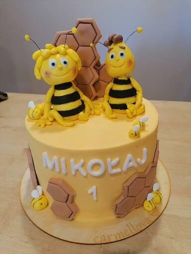 Żółty tort urodzinowy z imieniem Mikołaj i cyfrą 1, udekorowany figurkami pszczółek z bajki i motywem plastra miodu.