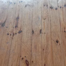 Stara, drewniana podłoga z widocznymi rysami i śladami użytkowania, przygotowana do renowacji. Widoczne sęki i naturalny rysunek drewna.