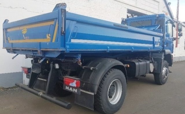 Niebieska wywrotka MAN z otwartą skrzynią ładunkową, zaparkowana w Łodzi, widok z tyłu i boku.