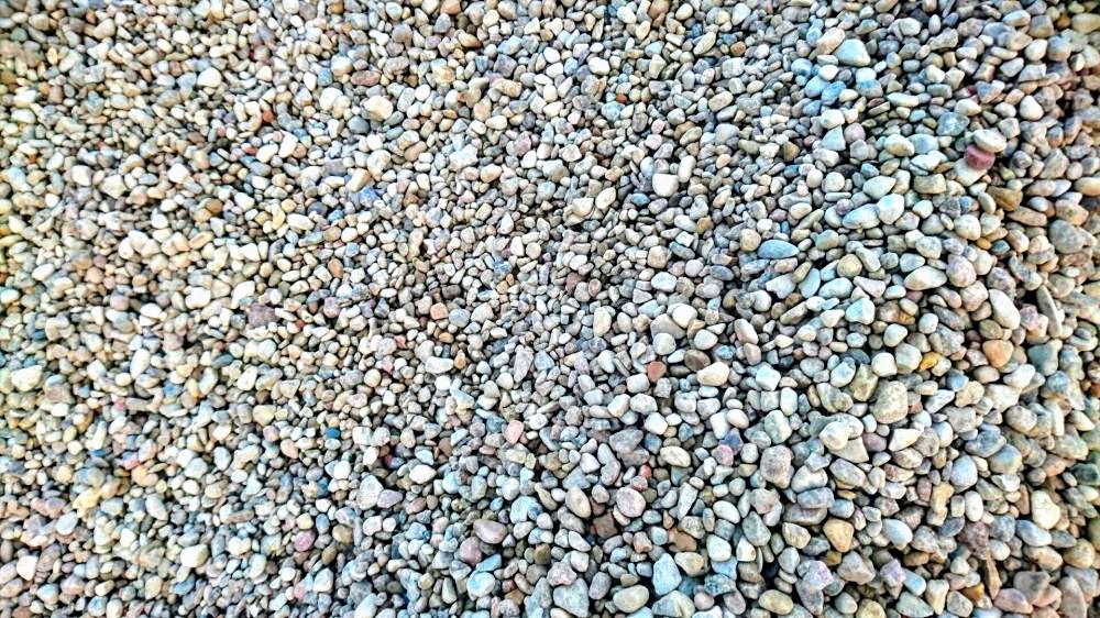 Nierównomierna faktura drobnego, jasnego żwiru z domieszką kamieni o różnych odcieniach szarości, beżu i błękitu, wypełniająca całą powierzchnię kadru.