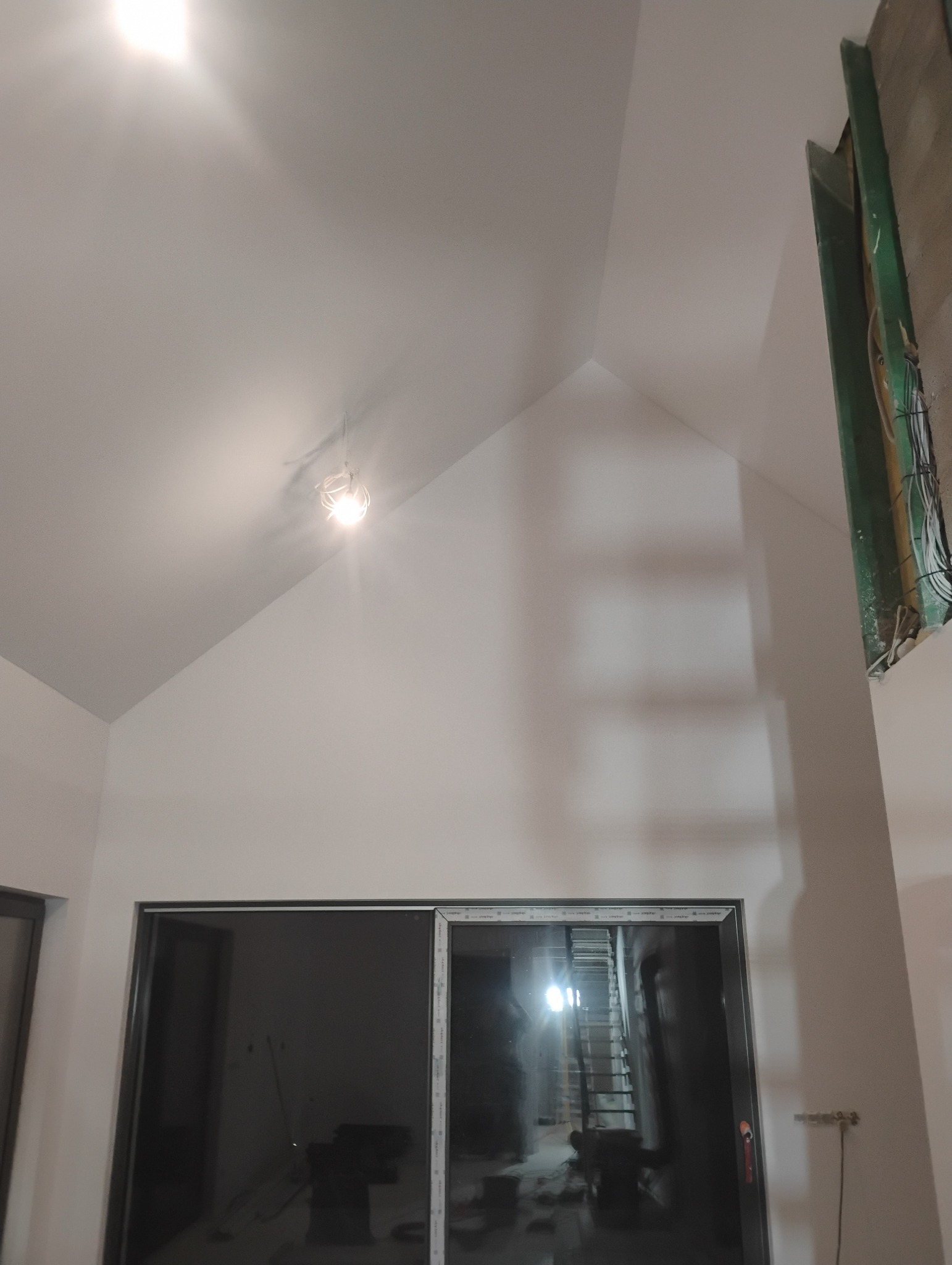 Wnętrze z gładzią na skośnym suficie i ścianach, widoczne okno przesuwne. Na suficie lampa. Fragment instalacji elektrycznej przy ścianie.
