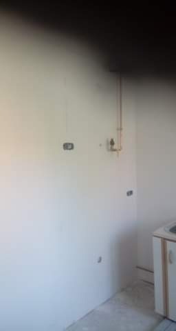 Wnętrze pomieszczenia w trakcie remontu, widoczne ściany przed malowaniem z wystającymi przewodami elektrycznymi i rurami, fragment szafki pod zlewem w rogu.