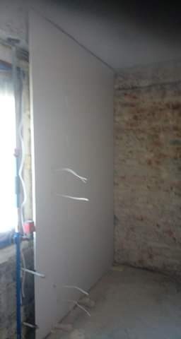 Montaż płyty karton gips na ścianie z widocznymi przewodami elektrycznymi, surowy stan wykończenia wnętrza.