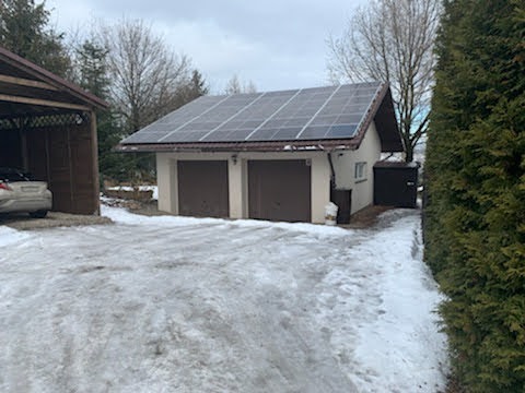 Dwustanowiskowy garaż z panelami słonecznymi na dachu, pokryty częściowo śniegiem podjazd.