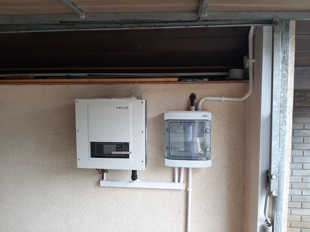 Zamontowany inwerter SOFAR i skrzynka zabezpieczeń na ścianie o fakturze baranka, z widocznymi białymi rurkami instalacyjnymi.