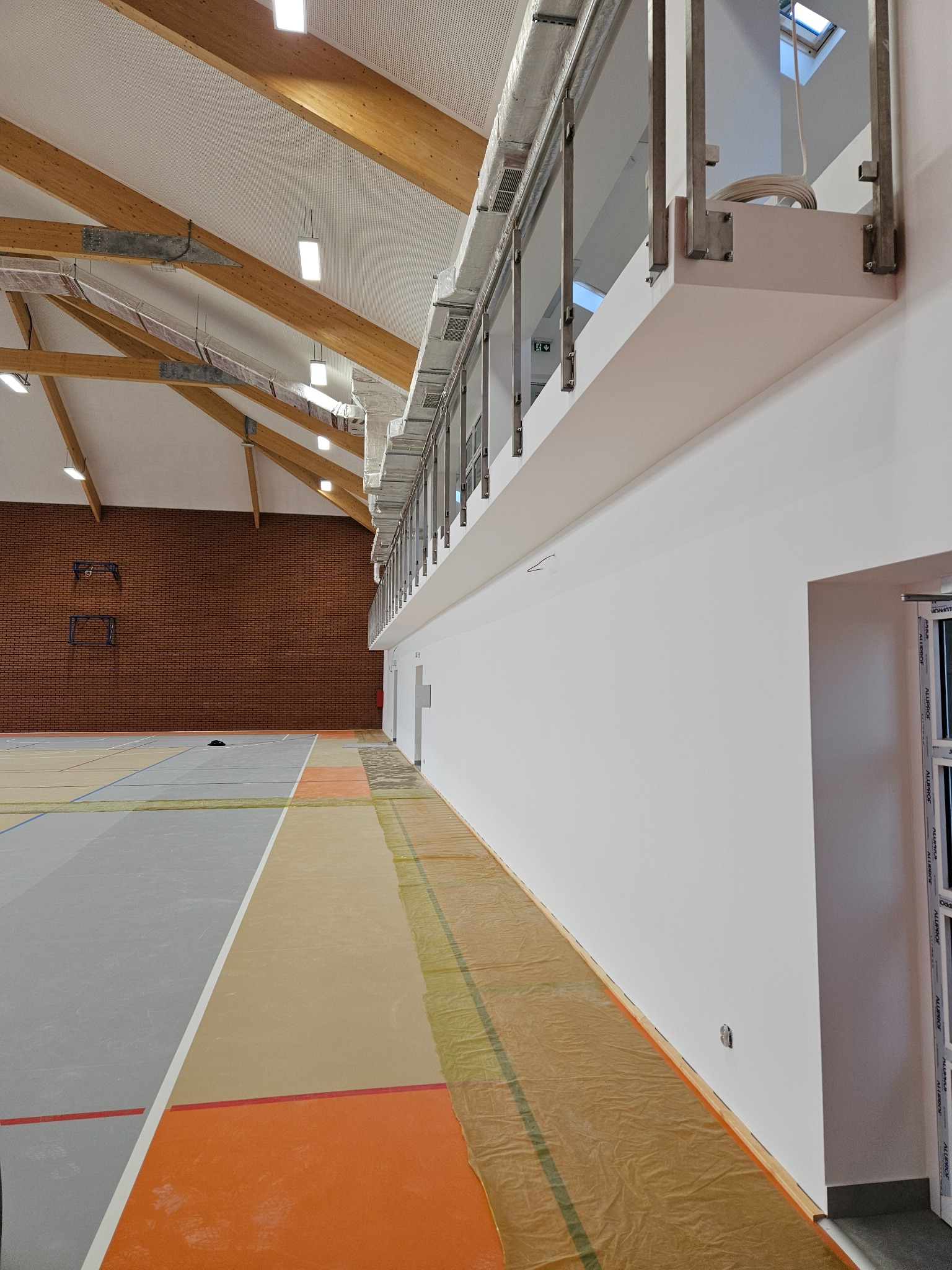 Sala gimnastyczna po remoncie, z zabezpieczoną folią podłogą, świeżo pomalowanymi ścianami i nowym oświetleniem sufitowym.