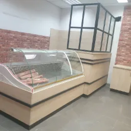 Nowa, drewniana lada chłodnicza z szybą i wędlinami w sklepie, z elementami zabudowy w tle, na tle ściany z cegły.