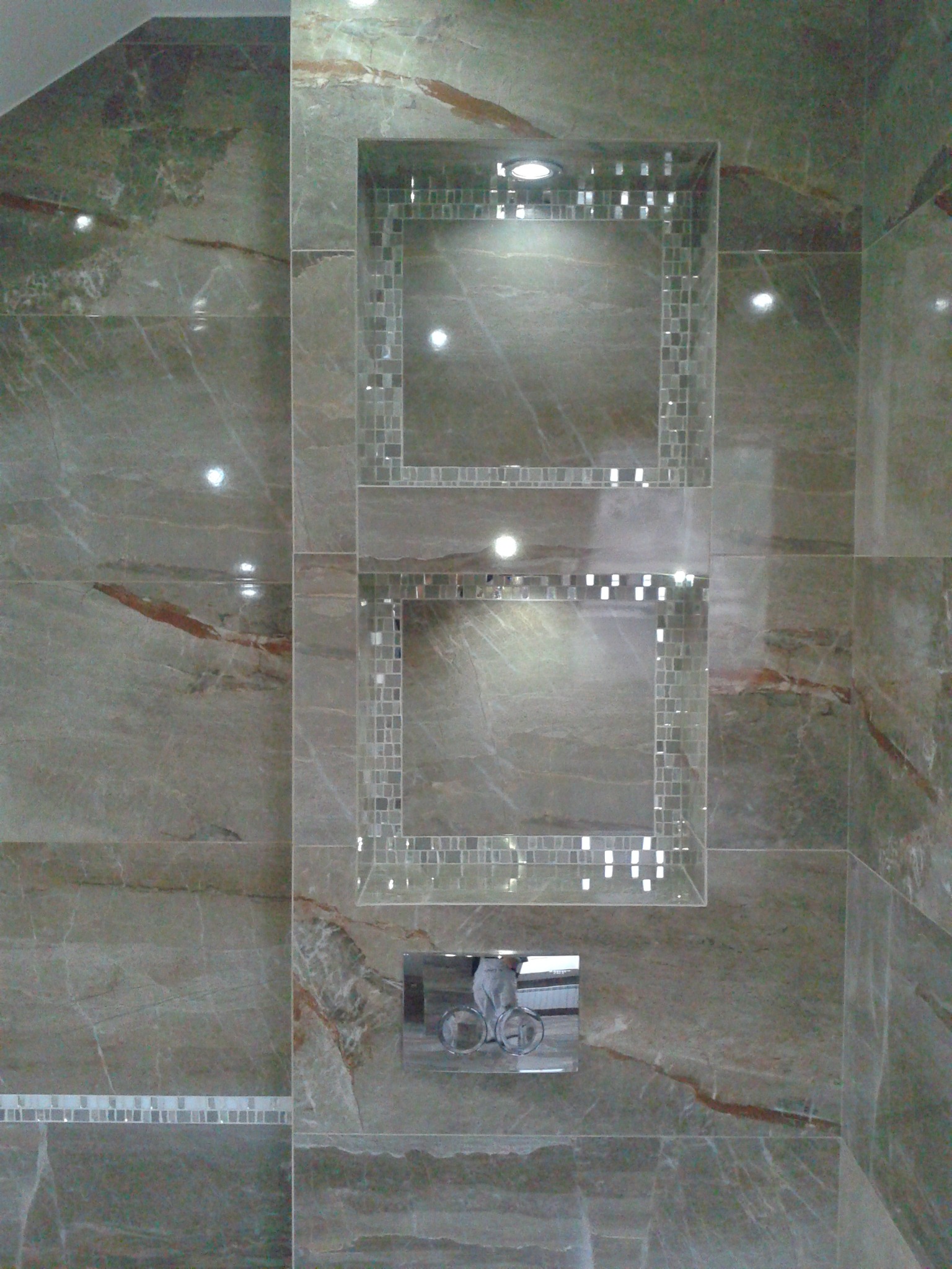 Wykończona łazienka z szarymi marmurowymi płytkami, wnękami z mozaiką i punktowym oświetleniem