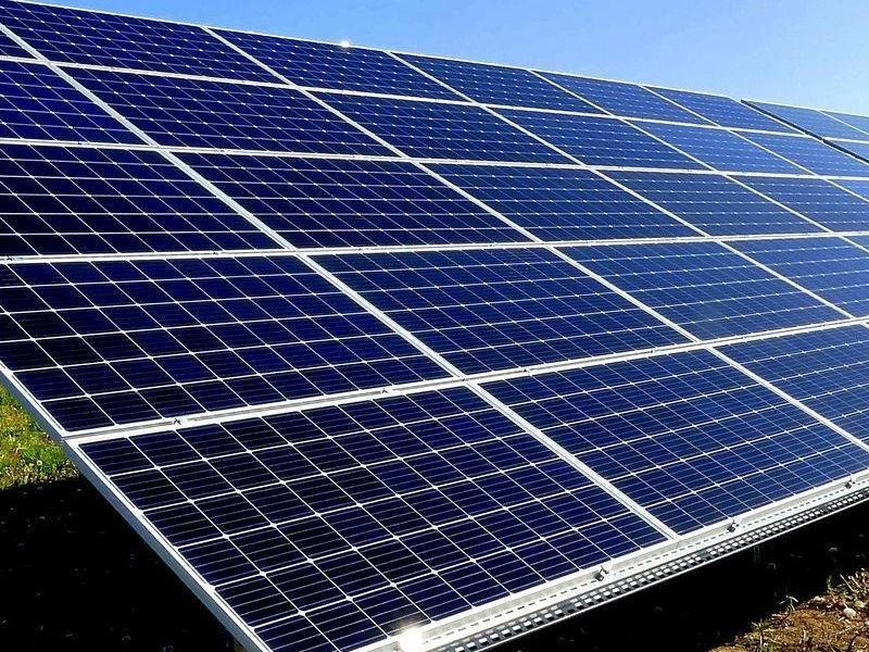 Rząd paneli słonecznych w instalacji naziemnej, widok z dołu pod kątem, błękitne niebo w tle.