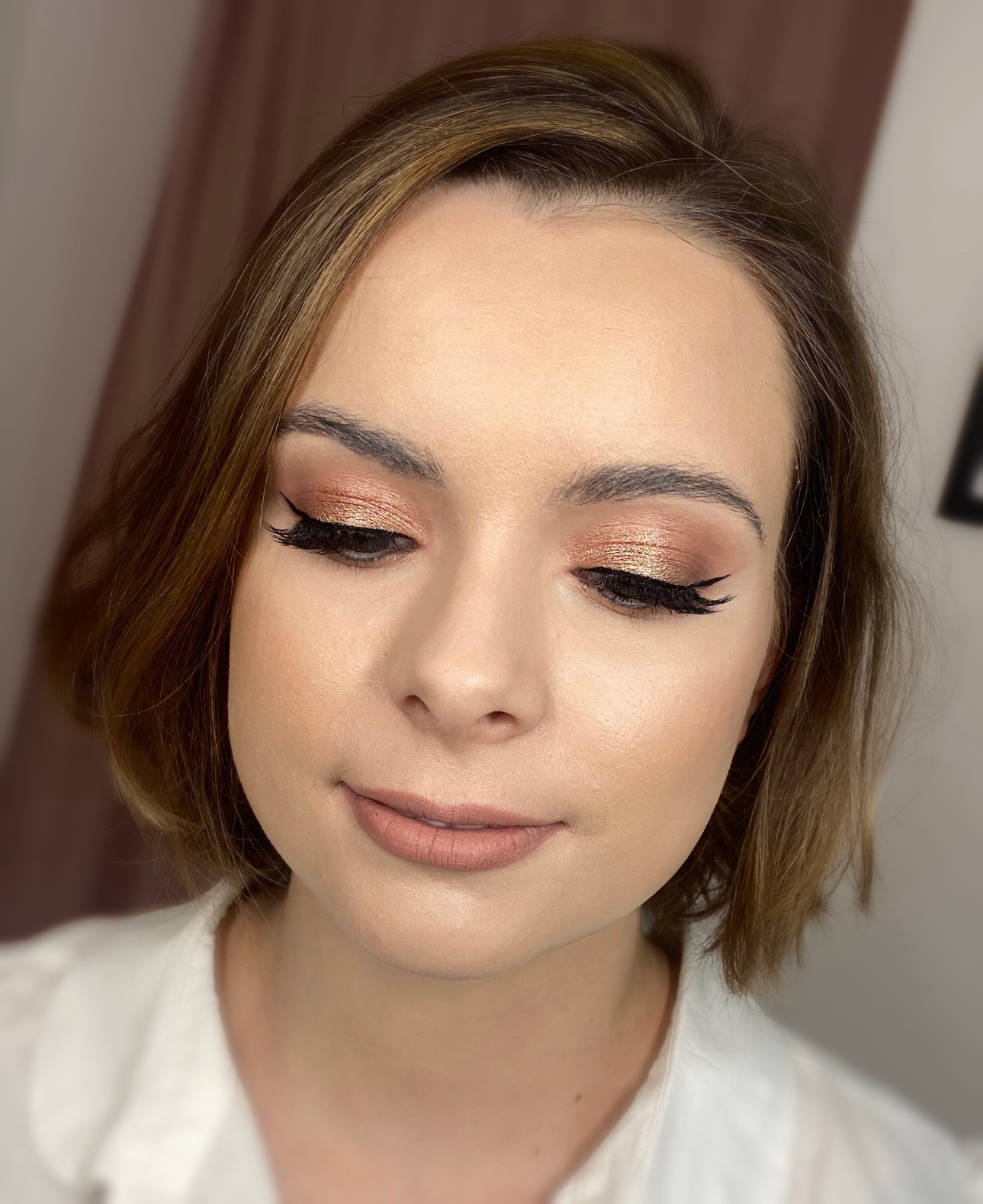 Portret kobiety z brązowo-złotym cieniem na powiekach i czarnym eyelinerem w stylu kociego oka; usta pomalowane matową pomadką w odcieniu nude.
