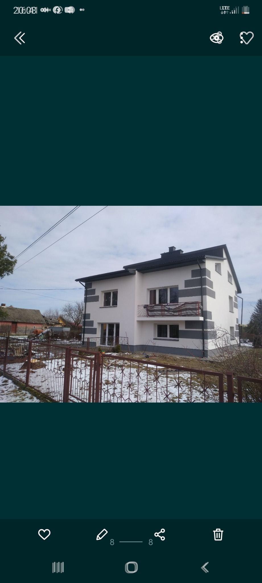 Dwukondygnacyjny dom po renowacji elewacji z białymi ścianami i szarymi pasami, widoczny zza metalowego ogrodzenia w zimowej scenerii.