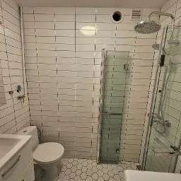 Biała łazienka z heksagonalną podłogą, prysznicem typu walk-in i umywalką z szafką, wykończona płytkami imitującymi cegłę.