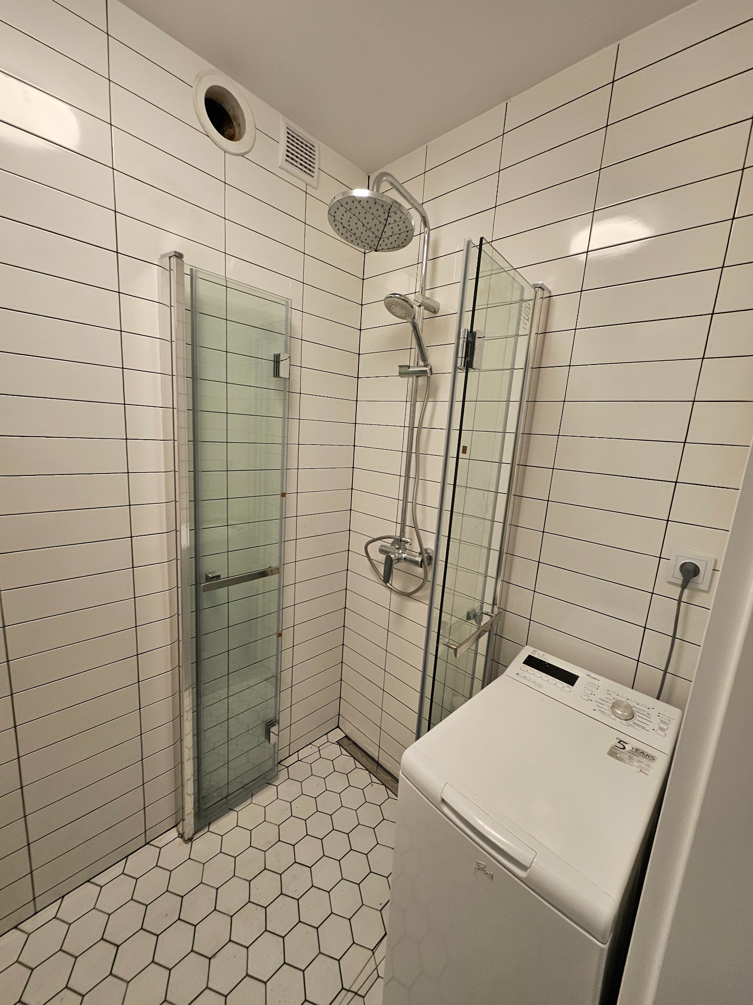 Nowoczesna łazienka z kabiną prysznicową, białe płytki w cegiełkę, heksagonalna podłoga i pralka Whirlpool.