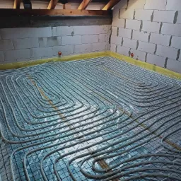 Instalacja ogrzewania podłogowego w surowym stanie, rury ułożone na folii aluminiowej z siatką, ściany z betonu komórkowego.