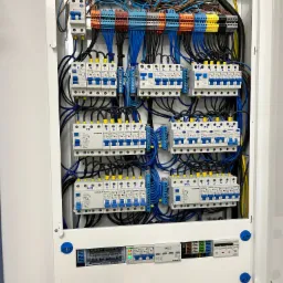 Rozdzielnica elektryczna Schrack z zainstalowanymi bezpiecznikami, przewodami o różnych kolorach i listwami zaciskowymi wewnątrz białej obudowy.